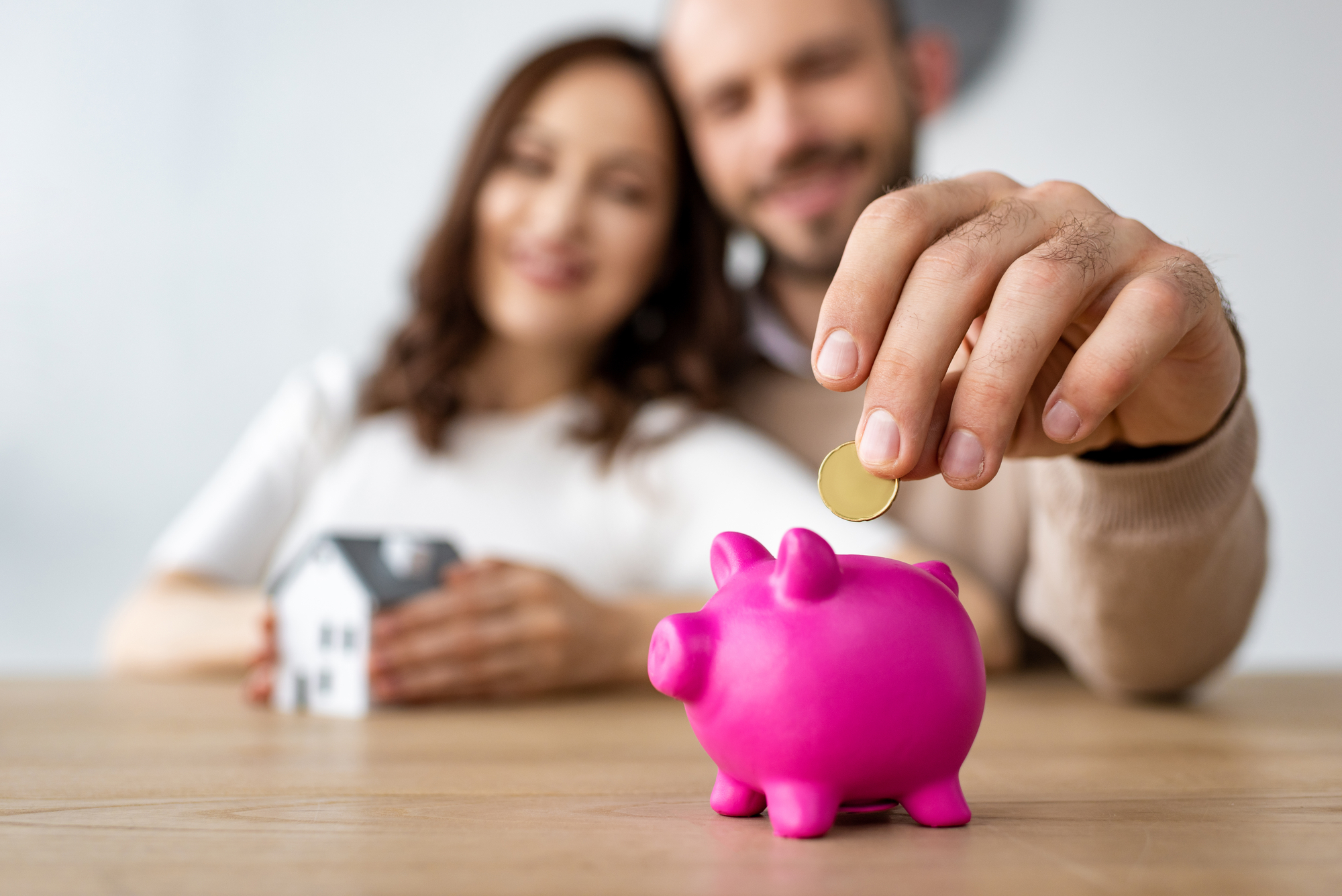 Selective focus of man putting coin in pink piggy bank and cheerful woman